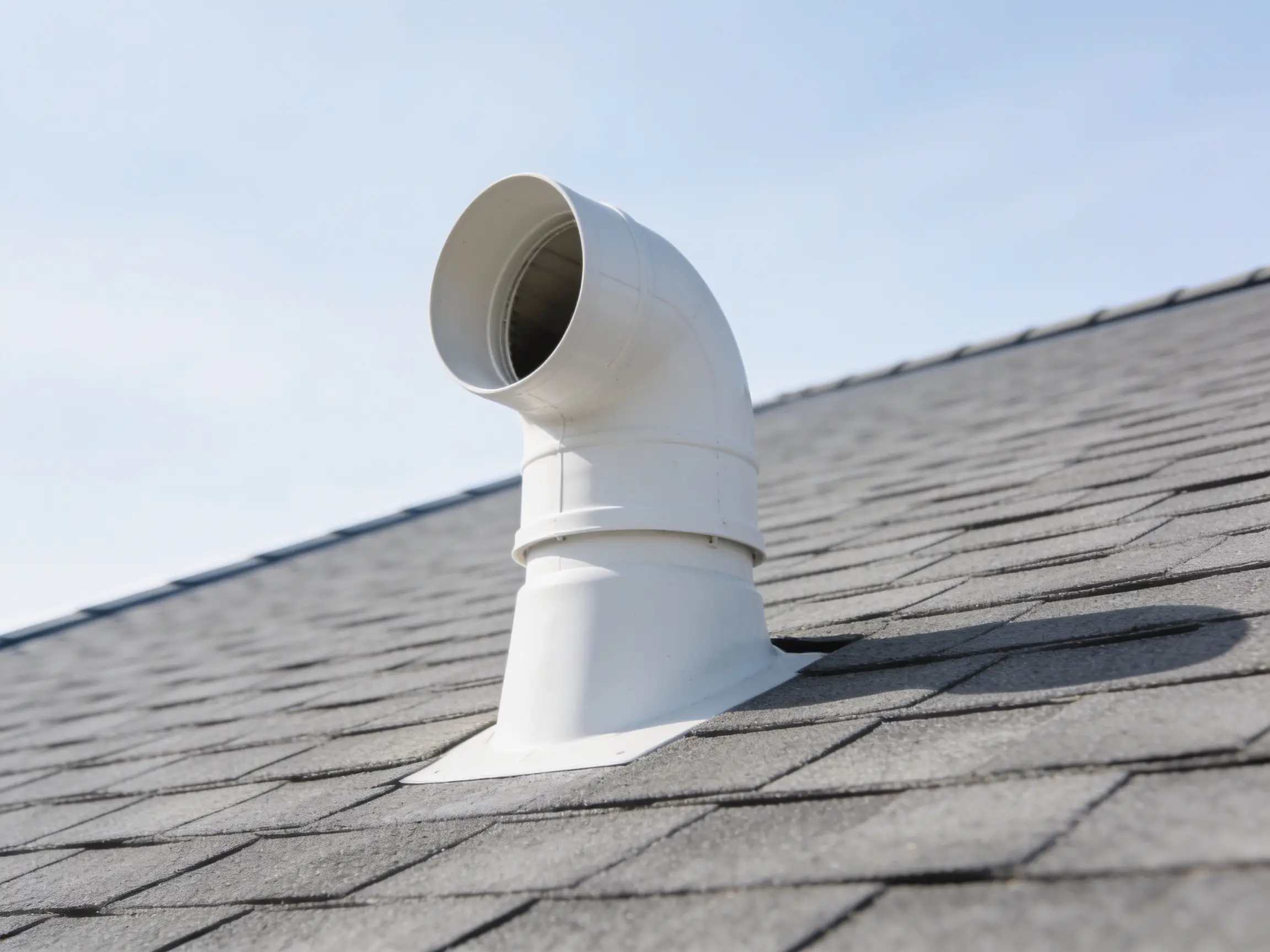Open plumbing vent pipe standing above a roof surface against the sky