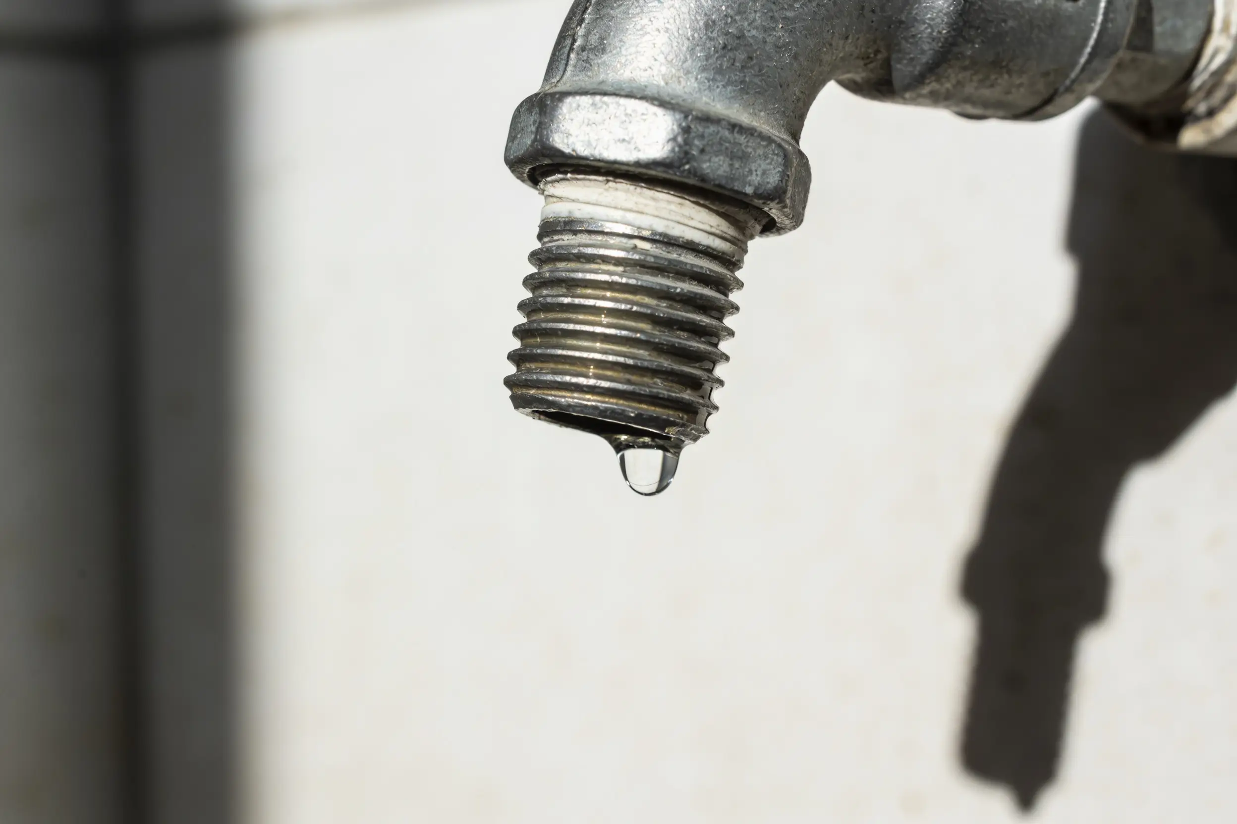 Clear bead of water hanging from the threaded joint of a galvanised steel pipe fitting